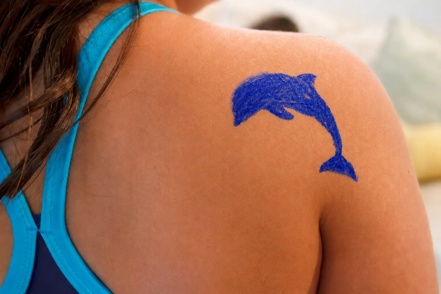 A bright blue dolphin drawn on a swimmer's shoulder